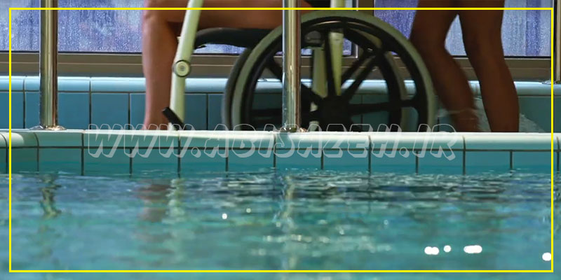 شخص معلول روی ویلچر و فیزیوتراپ در حال راه رفتن در کنار استخر فیزیوتراپی